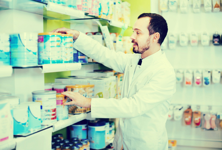 Cheerful positive male pharmacist looking for right medicine in pharmacyの写真素材