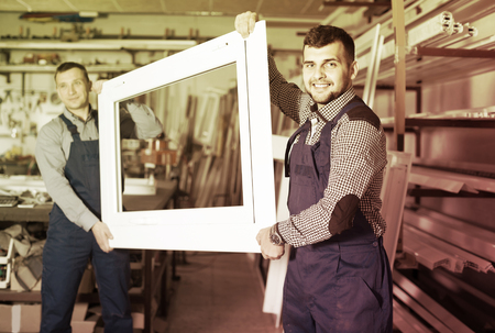Production happy workers in coverall with different    finished PVC profiles and windows at factoryの写真素材