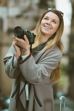 Young cheerful woman with a camera looking curious and taking pictures outdoorsの写真素材