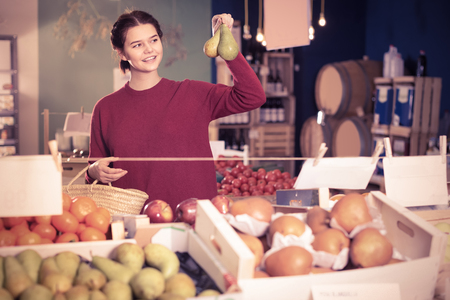 Portrait of happy english  brunette girl buying ripe pear in supermarketの写真素材