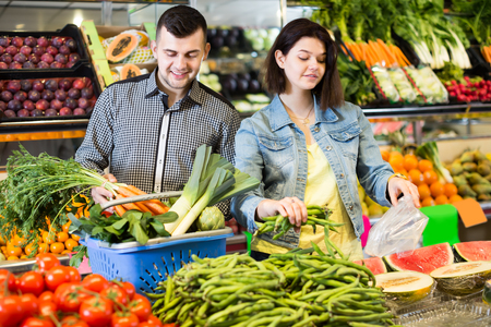 Young attentive couple choosing fresh vegetables in grocery shopの写真素材