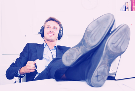 Portrait of young relaxed man in formal wear listening music in officeの写真素材