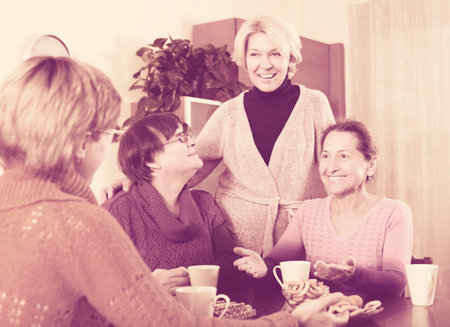 Happy mature female having cup of hot tea indoor and smiling
