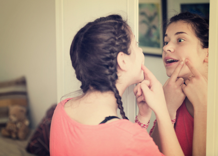 Young girl cleaning pores in front of mirror at homeの写真素材
