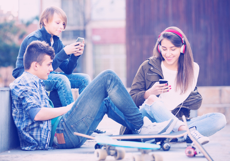 Three teenagers with smartphones and skateboards  in autumn day outdoorsの写真素材
