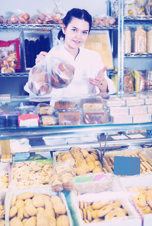 Young saleswoman posing with cookies at counter in sweets shopの写真素材