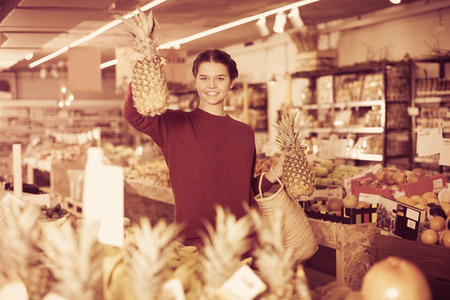 Portrait of brunette smiling girl buying ripe pineapple in supermarketの写真素材