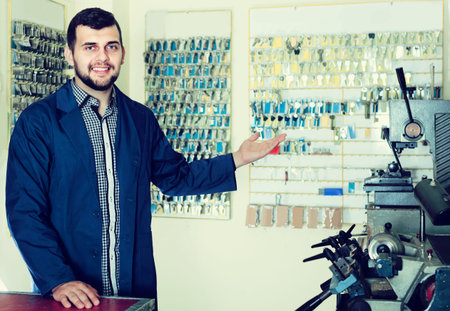Smiling american  male worker showing his tools for making keys in workshop