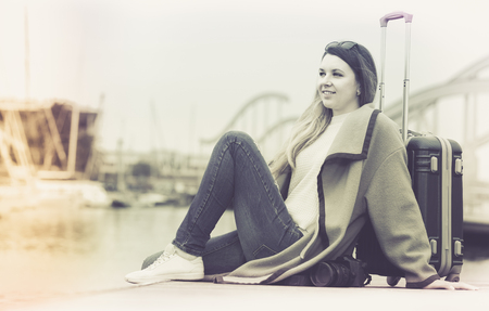 Happy young american woman with luggage  posing at quay and smilingの写真素材