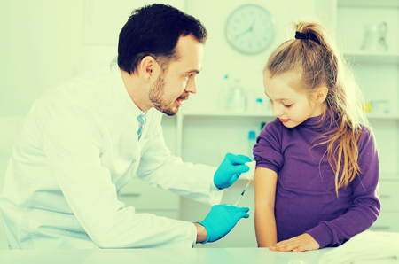 Young male doctor ready to make injection to teenage female visitor in hospitalの写真素材