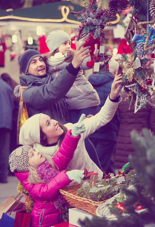 Smiling young parents with two little daughters choosing X-mas decorations in market. Focus on womanの写真素材