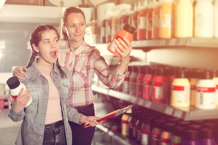 Cheerful mother and daughter holding glass jar with color paint in art shopの写真素材
