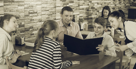 Nice hospitable waitress helping visitors with menu taking order in cafeの写真素材