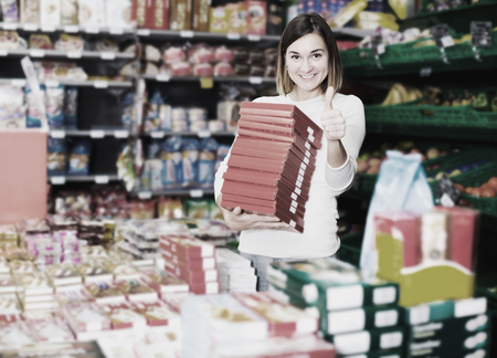 Smiling young woman choosing delicious sweets in supermarketの写真素材