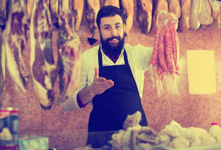 Young man seller showing different sausages in butchers shopの写真素材