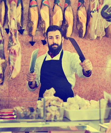 Smiling positive man seller preparing meat to sell in butcher’s shop