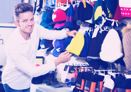 Young man choosing new knit cap in sports storeの写真素材