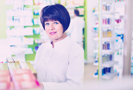 Portrait of diligent female druggist in white coat working in pharmacyの写真素材