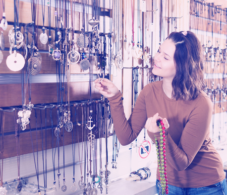 Young girl seller offering colored necklaces and pendants in the storeの写真素材