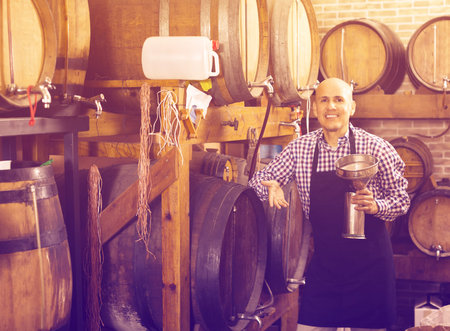 Joyful mature man wearing apron holding wine in wine houseの写真素材