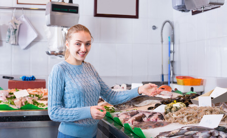Cheerful young housewife selecting cooled fish at fisheryの写真素材