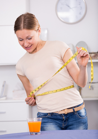 Smiling young woman measuring waist with yellow tapeの写真素材