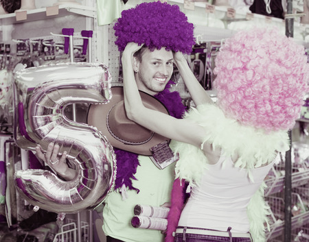 Cheerful smiling glad family couple preparing for fest and choosing clown wigsの写真素材