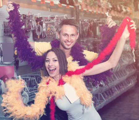 Smiling young couple showing colorful boa in storeの写真素材