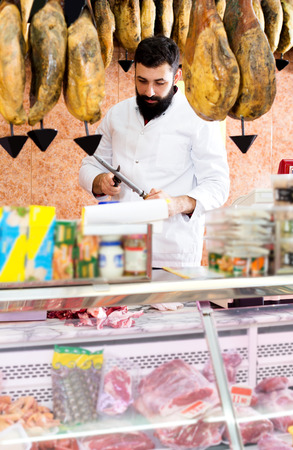 Young male seller cutting meat to sell in butchers shopの写真素材