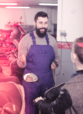 Smiling male worker assisting female customer in repairing motorcycle in workshopの写真素材