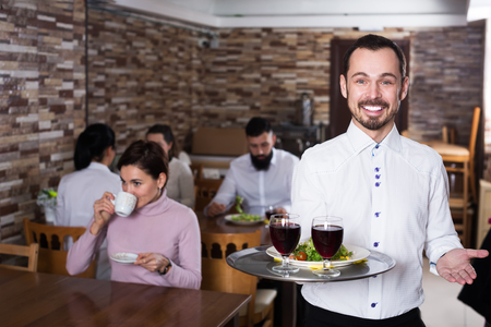 Young man waiter demonstrating rustic restaurant to visitorsの写真素材