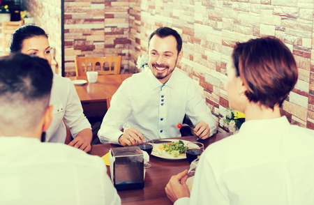 group of glad friends eating at restaurant table and chattingの写真素材