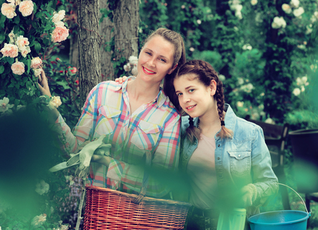 happy european female with long curly hair and girl standing near roses flower outdoorsの写真素材