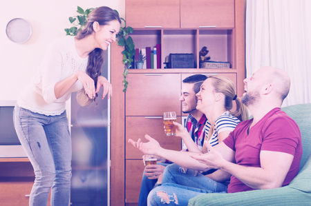 Positive adult friends hanging out with beer and jokes at homeの写真素材