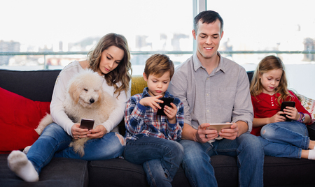 Young happy family playing with their smartphones together at homeの写真素材