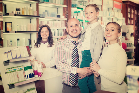 Cheerful smiling family of three persons getting help of a pharmacist at pharmacyの写真素材
