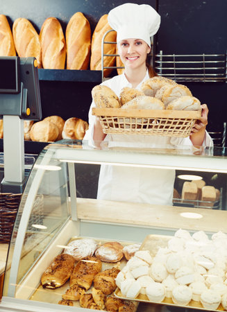 Portrait of young female bakery worker offering delicious bread in bakery