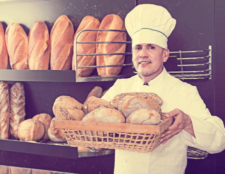 positive bakery male worker with tasty and fresh bread products on counter in the shopの写真素材