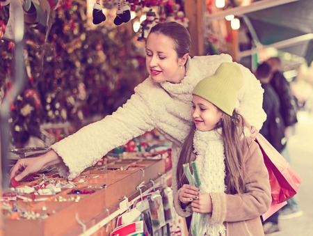 Smiling happy mother with daughter choosing gifts in Christmas marketの写真素材