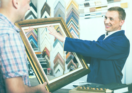 cheerful smiling man worker chatting with customer about picture frame details on counter in atelierの写真素材