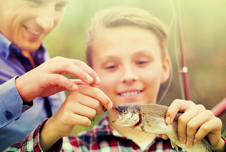 Glad teenager boy holding and looking at a fish on hookの写真素材