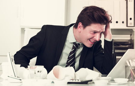 Portrait of young man in stress sitting at the table in the officeの写真素材