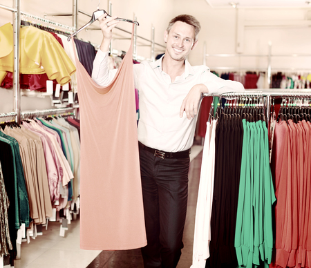 Young smiling man helping girlfriend to choose gown in the clothes storeの写真素材