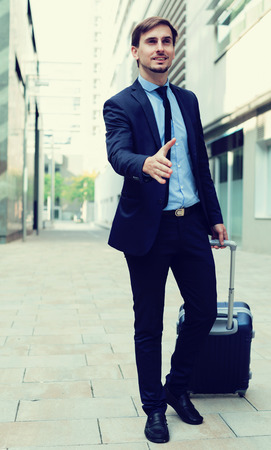 Portrait of cheerful male going with bag and offering one's handの写真素材