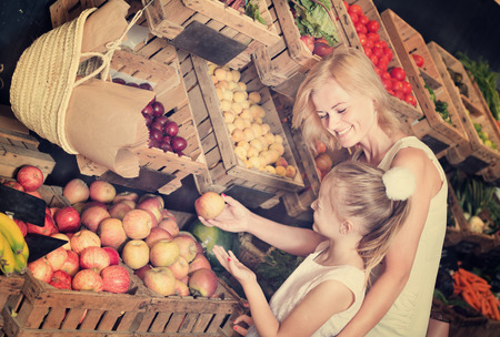 Glad young mother with daughter shopping various fruits at food store. Focus on womanの写真素材