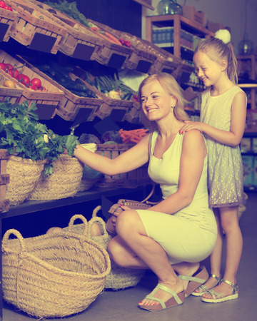 Portrait of glad woman and girl buying fresh greens in grocery shopの写真素材
