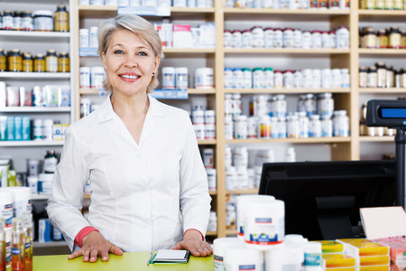 Aged woman seller noting assortment of care products in shopの写真素材