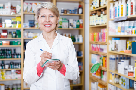 Senior woman seller writing assortment of care products in storeの写真素材
