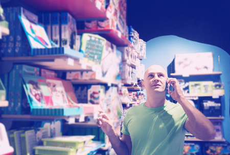 Positive adult man in toy store calls by telephone to the wife to consultの写真素材