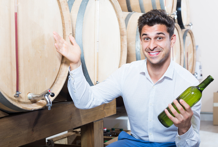 Smiling man customer having bottle of wine in shop with woodsの写真素材